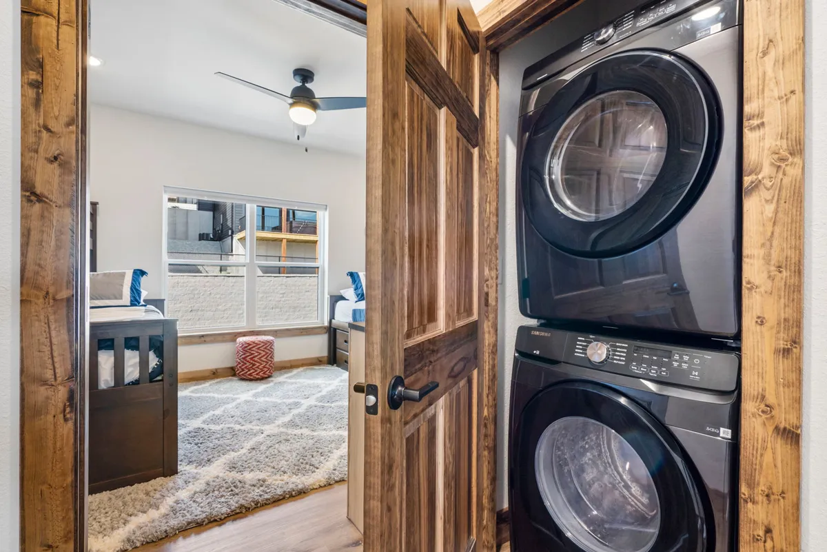 A practical yet cozy space featuring a stacked washer and dryer just off a bedroom, with natural light streaming in. The laundry facilities are easily accessible, making extended stays effortless for families.