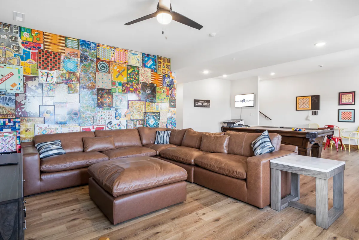 This image features a vibrant game room with a large sectional sofa, colorful wall art, and a pool table as the centerpiece. The setup exudes a casual and playful atmosphere, inviting guests to gather for game nights or friendly competitions. The visibility of both lounging space and the billiards table highlights the versatility of the room for both active and relaxed entertainment.