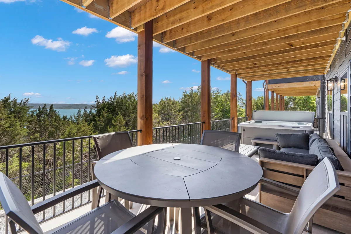 An inviting exterior shot of a spacious deck overlooking natural scenery, featuring an outdoor dining table and a private hot tub. Plush seating and the scenic view make the space ideal for both relaxation and group activities like stargazing or sharing a meal outdoors.