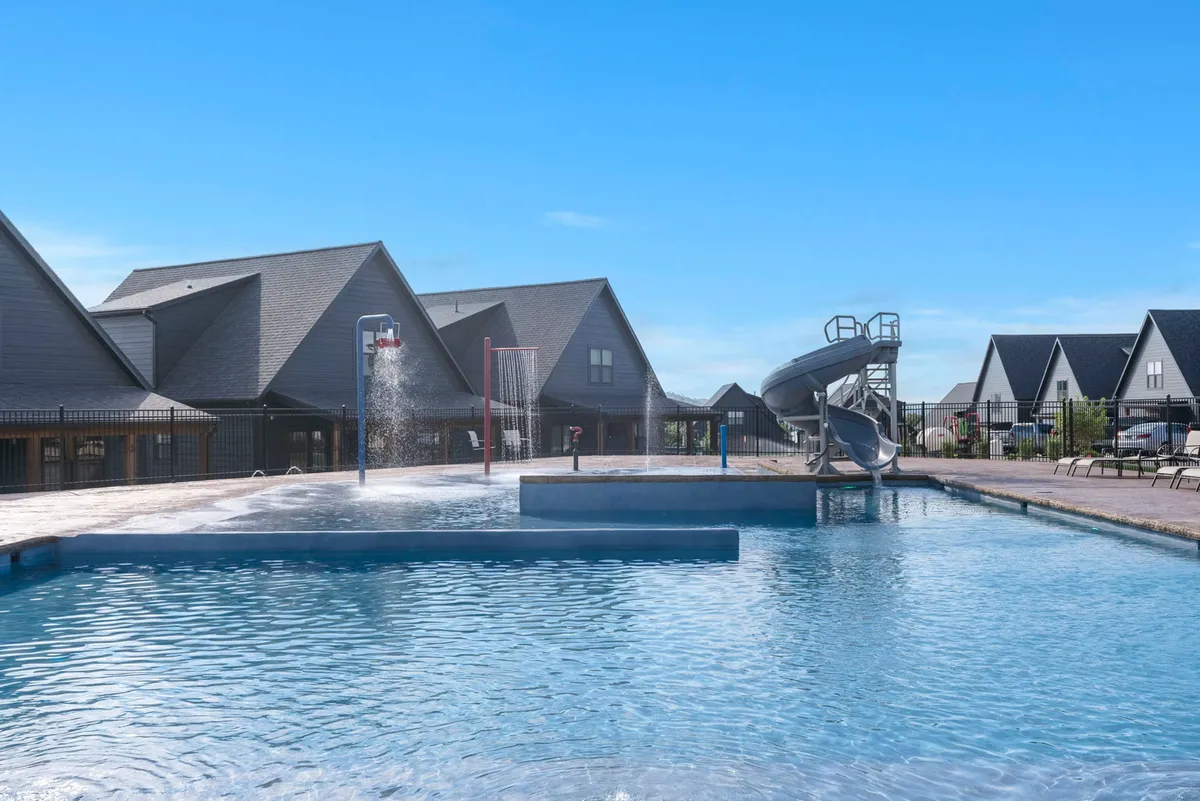 A joyful exterior scene showing a large swimming pool with a winding water slide, surrounded by modern buildings and an array of lounge chairs. Families and children enjoy time in and around the pool, emphasizing the communal and social environment.