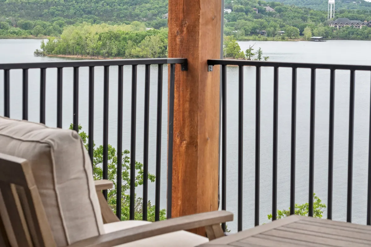 An inviting exterior view from a wooden-railed balcony overlooks a calm lake and lush green landscape, with comfortable seating arranged to enjoy the natural surroundings. The peaceful mood and connection to nature are front and center.