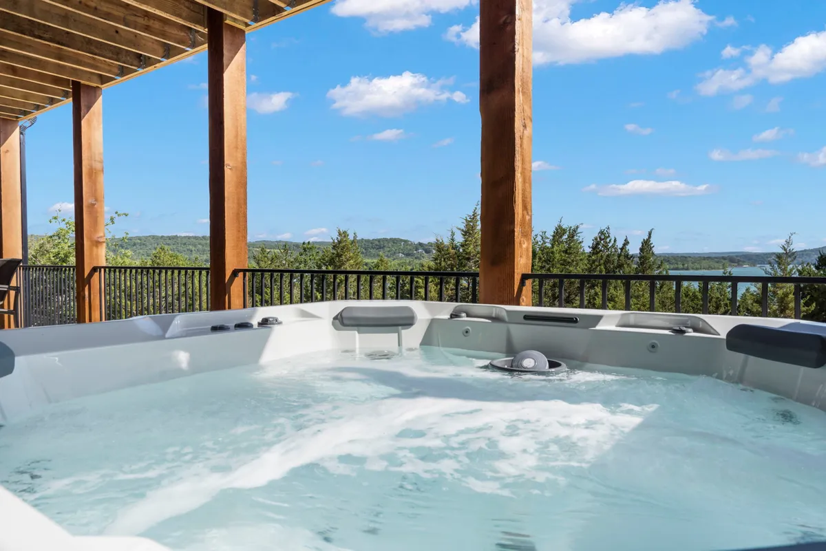 A serene hot tub nestled on a private lower deck, framed by wooden beams and overlooking a peaceful lake view. The setup is inviting for relaxation, stargazing, and late-night conversations.