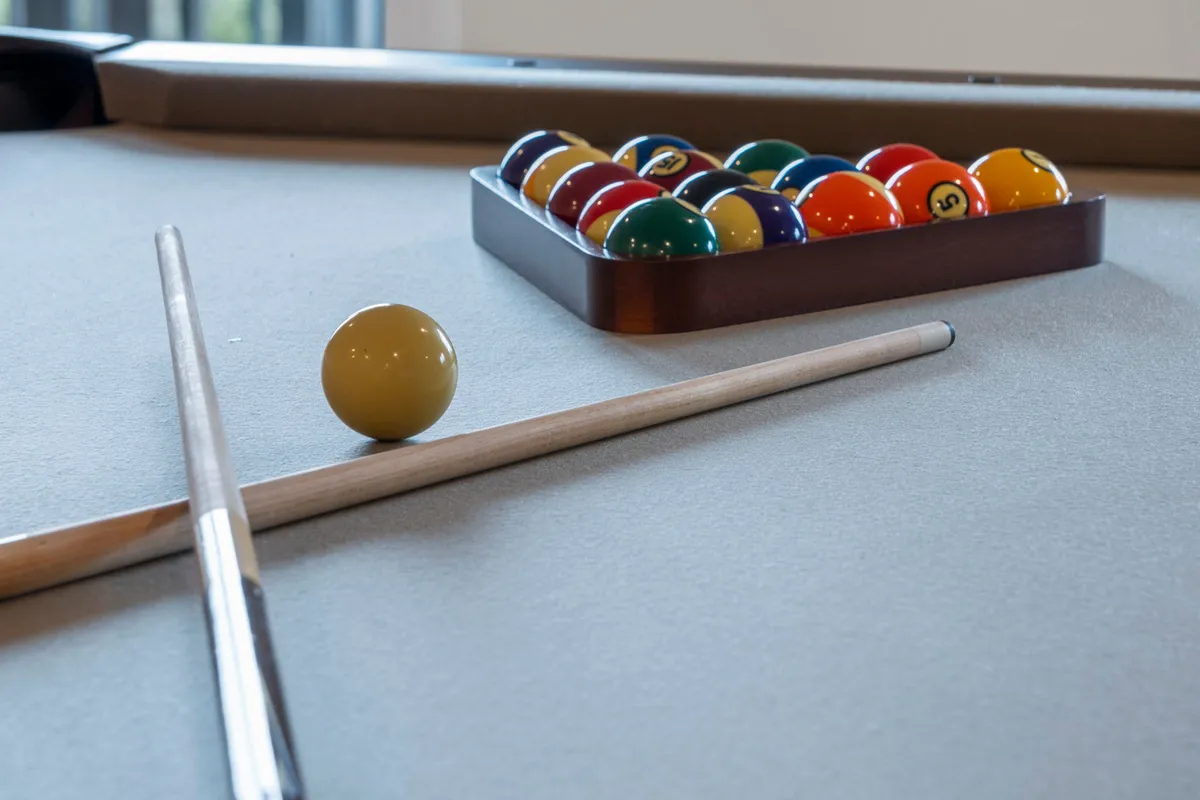 A close-up shot of a pool table with cue sticks and a full set of billiard balls ready for play. The scene captures the anticipation before a game begins and highlights the playful and social nature of the space.