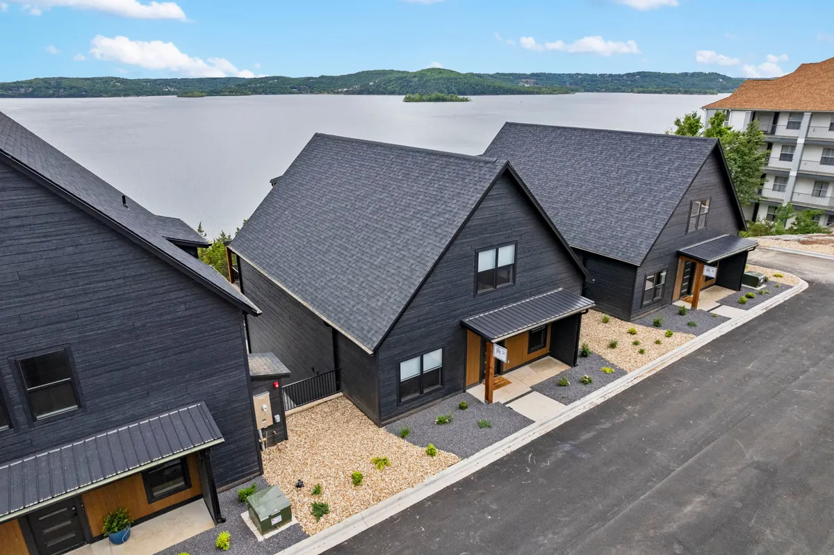 This exterior shot depicts modern black houses set against a backdrop of the lake, with a landscaped pathway leading toward the water. The scene is peaceful and hints at easy access to both the lake and outdoor communal areas.