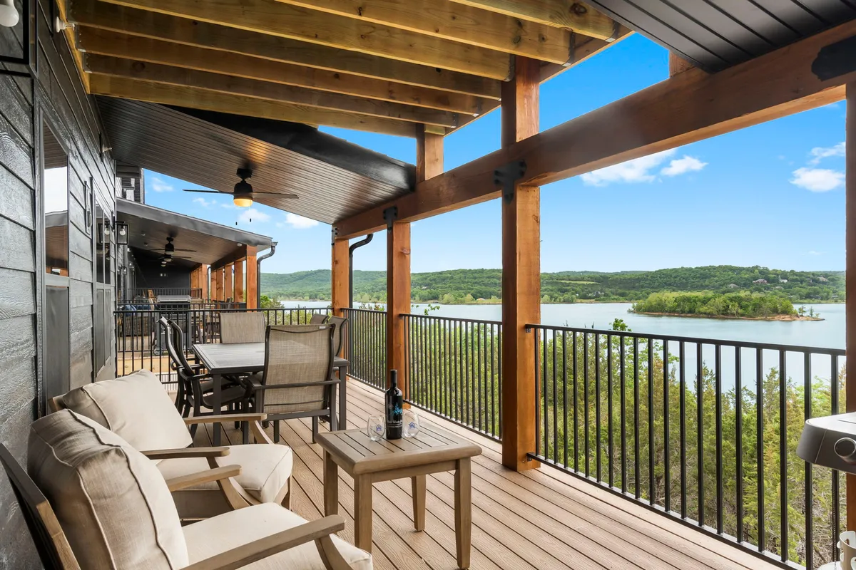 A serene exterior balcony scene with comfortable outdoor seating, wooden beams, and panoramic views of the lake. The setup is perfect for sunset conversations, quiet moments of reflection, or sharing drinks with friends while soaking in the tranquil ambiance.