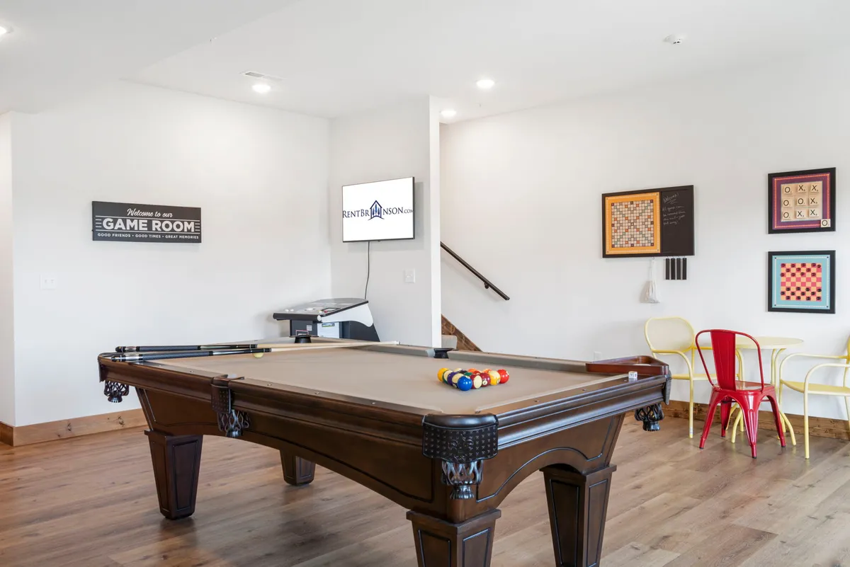 A vibrant interior game room filled with a pool table, colorful chairs, and a 'game room' sign, inviting guests to enjoy friendly competitions and social moments. Board games are also visible, highlighting the variety of entertainment options inside.