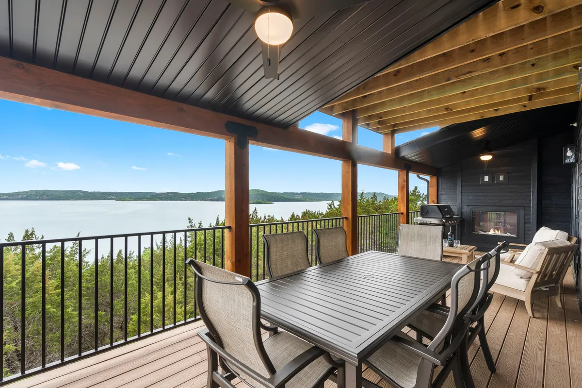 A spacious outdoor deck with a dining table set for alfresco meals, comfortable seating, and a fireplace. The scene overlooks the lake, inviting outdoor relaxation and gatherings as the sun sets or stars appear.